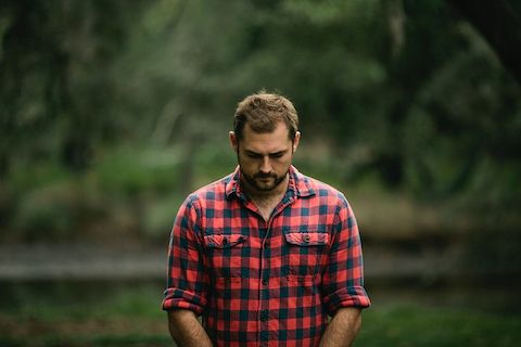 Man clasping his own hands together and looking downward, expressing sadness. 